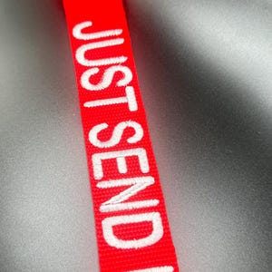 May include: A red fabric keychain with the white embroidered text "JUST SEND IT".