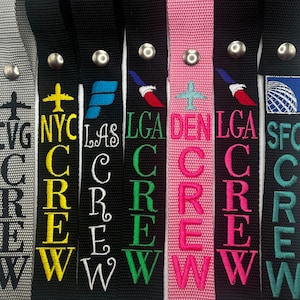 May include: Eight colorful luggage tags with the text "CREW" and airport codes, including CVG, NYC, LAS, LGA, DEN, SFO. The tags are made of black, gray, pink, and green fabric.