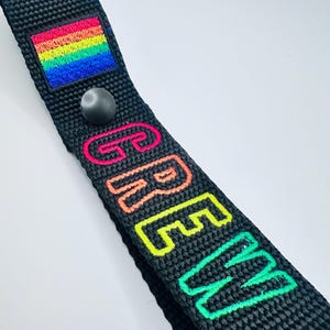 May include: Black strap with a rainbow flag and the word "CREW" embroidered in rainbow colors.