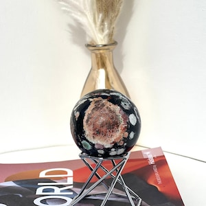 May include: A black and brown speckled sphere on a silver metal stand. The sphere is sitting on a magazine with the word "WORLD" printed on the cover.