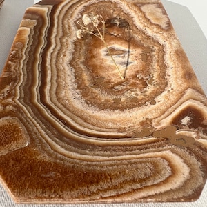 May include: A brown and white onyx serving tray with a decorative, wavy pattern. The tray has a slightly irregular shape and a smooth, polished surface.