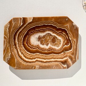 May include: A brown and white agate tray with a unique swirling pattern. The tray is made of natural stone and has a smooth, polished finish.