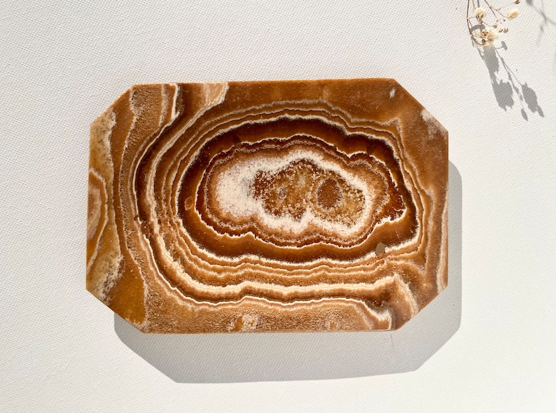 May include: A brown and white agate tray with a unique swirling pattern. The tray is made of natural stone and has a smooth, polished finish.