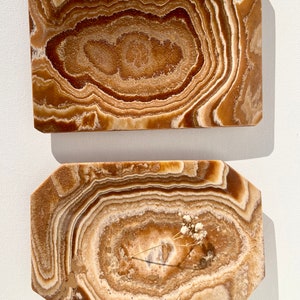 May include: Two rectangular trays made of brown onyx with a swirling pattern. The larger tray is plain, while the smaller tray has a dried flower sprig in the center.