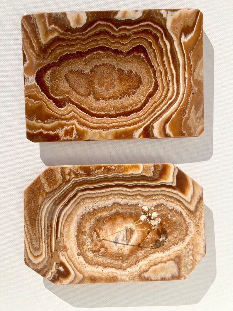 May include: Two rectangular trays made of brown onyx with a swirling pattern. The larger tray is plain, while the smaller tray has a dried flower sprig in the center.