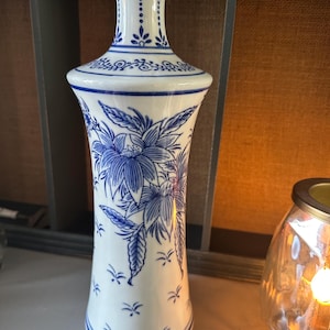 Könnte beinhalten: Eine weiße Keramikvase mit einem blauen und weißen Blumendesign. Die Vase hat einen schmalen Hals und einen breiten Boden.