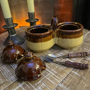 以下が含まれることがあります： ハンドル付きのヴィンテージ2セクションセラミック調味料サーバー、茶色とクリーム色の配色、および2つのマッチング蓋。 木製のハンドルが付いた2つの小さなスプーンと、火の灯ったキャンドルが付いた2つの燭台も存在します。