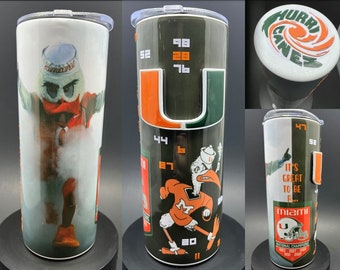 May include: A green and orange tumbler with a University of Miami logo and mascot. The tumbler has the words "It's Great To Be A... Miami" and "National Champions 1983 1987 1989 2001" printed on it.