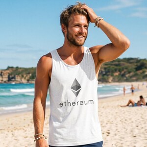 May include: White vest top featuring the Ethereum logo and text. The top is paired with navy blue shorts. The image is taken on a sunny beach with the sea in the background.
