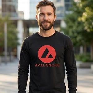 Op de afbeelding: Zwart shirt met lange mouwen met een rood cirkelvormig logo en het woord "AVALANCHE" in het rood. Het logo toont een rode cirkel met een driehoek en een kleinere driehoek erin. Het shirt is gemaakt van zacht materiaal.
