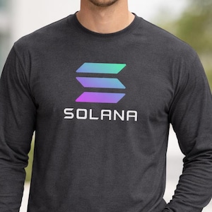 Peut inclure: T-shirt à manches longues gris foncé avec le logo Solana en dégradé vert, bleu et violet. Le mot "SOLANA" est imprimé en blanc en dessous. Le t-shirt est fait d'une matière douce.