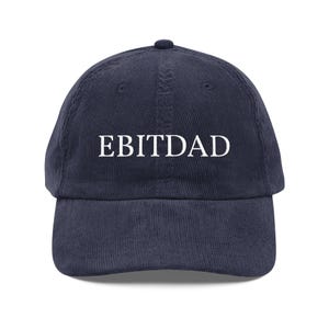 Könnte beinhalten: Marineblaue Cord-Baseballkappe mit dem weißen Text "EBITDAD" auf der Vorderseite. Die Kappe hat einen gebogenen Schirm und einen Knopf oben. Ein lässiges Accessoire.