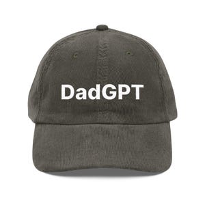 May include: A dark olive green corduroy baseball cap with the text "DadGPT" in white block letters across the front. The cap has a curved brim and a small button on top.