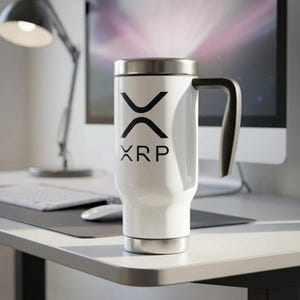 Puede incluir: Taza de viaje blanca con asa negra y tapa y base plateadas. La taza presenta el logotipo de XRP en negro. La taza está sobre un escritorio blanco con una computadora y una lámpara en el fondo.