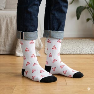 Puede incluir: Calcetines blancos con un diseño geométrico rojo repetido. Los calcetines tienen talones y dedos negros. Los calcetines se usan con jeans azules.