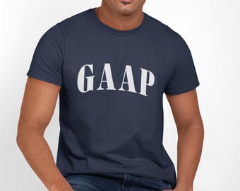 May include: Navy blue t-shirt with the word "GAAP" in white, arched lettering. The model is wearing blue jeans and is seated. The shirt is a classic crew neck style.