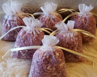 May include: Six small white organza bags filled with pink and white dried flower petals. The bags are tied with white satin ribbon.