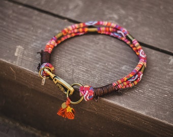 May include: A colorful dog collar with a woven design in red, orange, blue, and white. The collar has a brass clasp and a small tassel.
