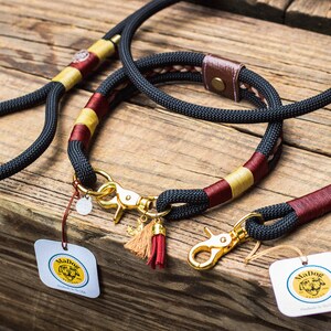 Puede incluir: Un juego de correa y collar para perros negro con herrajes dorados. El collar y la correa presentan detalles en burdeos y dorado. El conjunto incluye una correa y un collar a juego, con una etiqueta "MaDog".