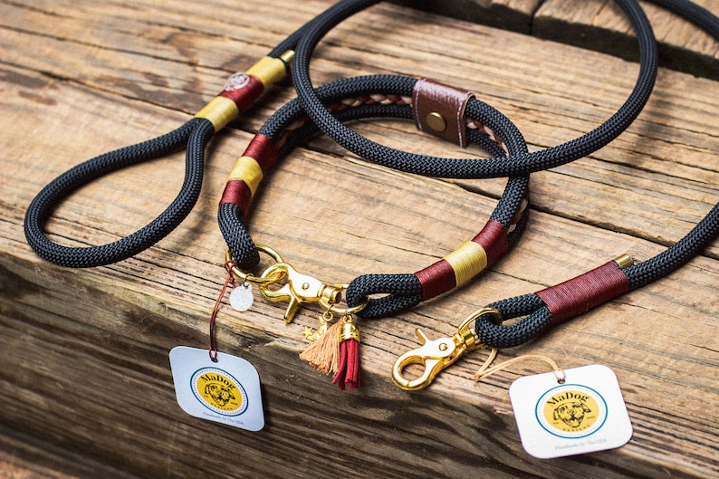 Puede incluir: Un juego de correa y collar para perros negro con herrajes dorados. El collar y la correa presentan detalles en burdeos y dorado. El conjunto incluye una correa y un collar a juego, con una etiqueta "MaDog".