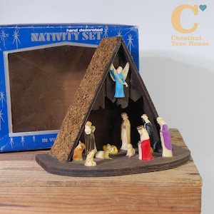 Può includere: Un presepe vintage con una stalla in legno e statuine. La stalla ha un tetto strutturato e una base marrone scuro. Le statuine includono un angelo, Maria, Giuseppe e i tre re magi. La scatola recita "Nativity Set".