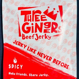 May include: White and red bag of Three GIngers Beef Jerky. The bag features the text "JERKY LIKE NEVER BEFORE" and "SPICY". The bag contains 3 oz (85g) of jerky.
