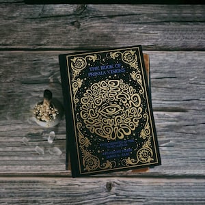 Może przedstawiać: Czarna książka z złotym wzorem przedstawiającym oko i tekst "The Book of Prisma Visions: An Exploration of the Tapot Arcana" autorstwa Katherine TỪMis i Jamesa R. Eads.