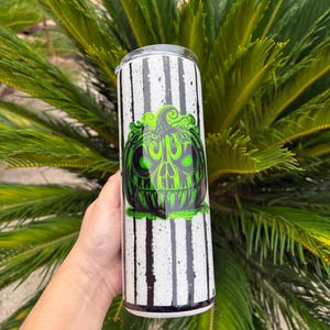 May include: A tall, stainless steel tumbler with a black and white striped pattern. The tumbler features a green and black graphic of a skull-like pumpkin. The design is likely for Halloween or a similar theme.