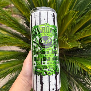 May include: A cylindrical tumbler with a black and white striped pattern. The tumbler features a green and black label with the text "Jack Skellington Mold Time" and "Halloween Town". The label also includes the text "Deadly Nightshade" and "Pumpkin King Distillery".