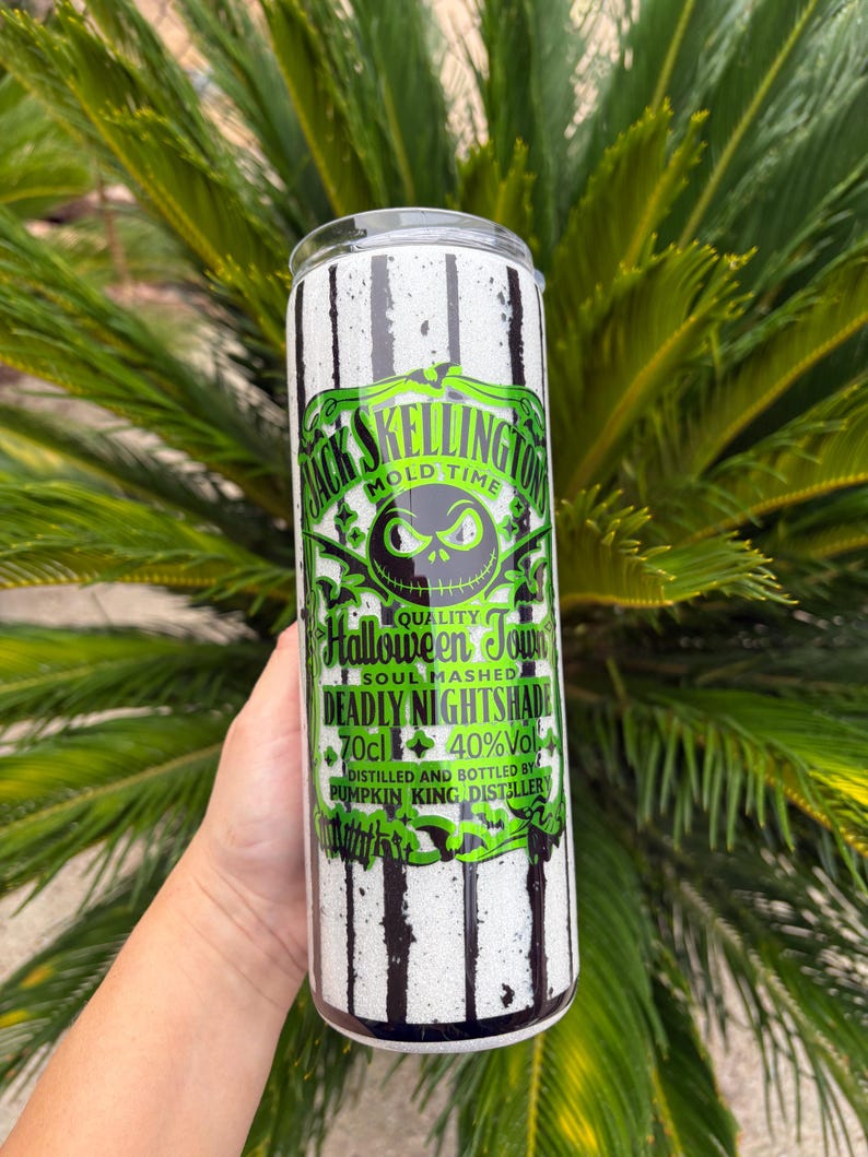 May include: A cylindrical tumbler with a black and white striped pattern. The tumbler features a green and black label with the text "Jack Skellington Mold Time" and "Halloween Town". The label also includes the text "Deadly Nightshade" and "Pumpkin King Distillery".