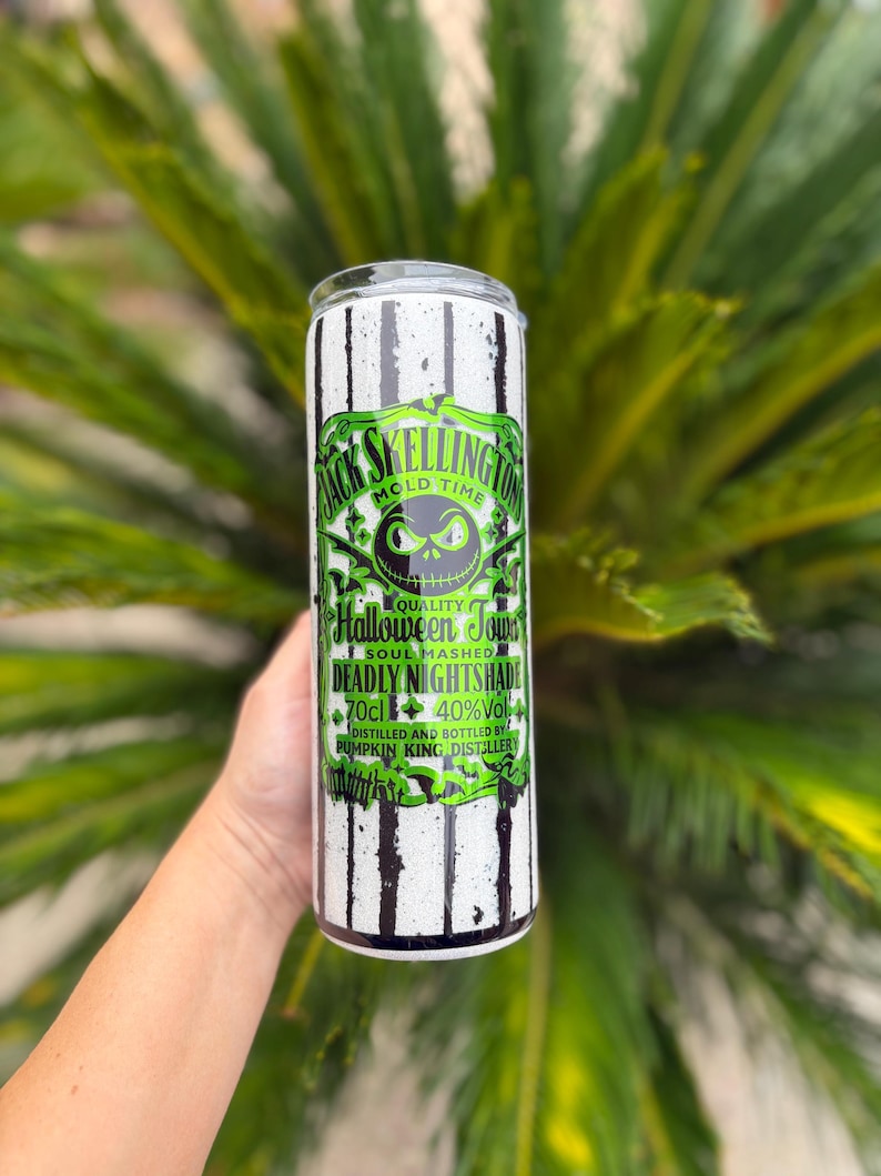 May include: A tall, cylindrical tumbler with a black and white striped pattern. The tumbler features a green and black label with the text "Jack Skellington Mold Time" and "Halloween Town". The label also includes the text "Deadly Nightshade" and "70cl 40%Vol".