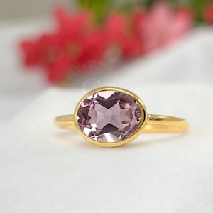 May include: A gold ring with a light purple oval gemstone. The ring is set in a simple, elegant style.