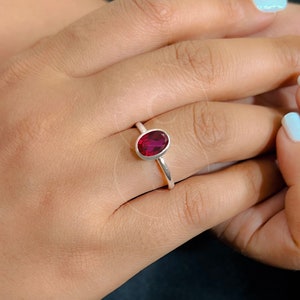 Op de afbeelding: Een zilveren ring met een dieprode ovale edelsteen. De ring zit aan een vinger.