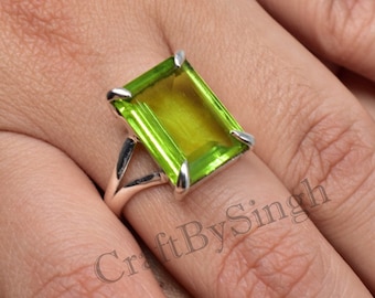 May include: A silver ring with a large, emerald-cut green peridot gemstone. The ring is set in a simple, elegant design.
