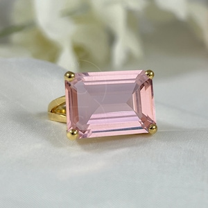 May include: A gold ring with a large, rectangular, light pink gemstone.