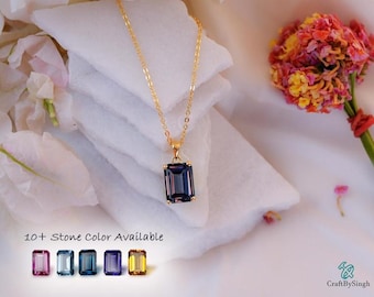 Puede incluir: Un collar de cadena en tono dorado con un colgante rectangular de color morado oscuro en talla esmeralda. El texto 10+ Stone Color Available aparece sobre una fila de cinco pequeñas muestras de piedras rectangulares en rosa, azul claro, azul oscuro, morado y amarillo.