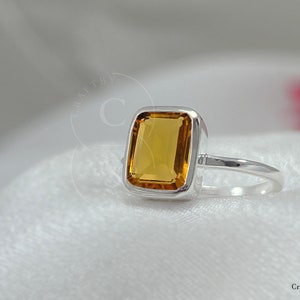 May include: A silver ring with a square-shaped, orange-brown gemstone.