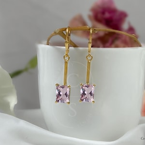 May include: A pair of gold earrings with pink square-shaped gemstones hanging from a gold chain.