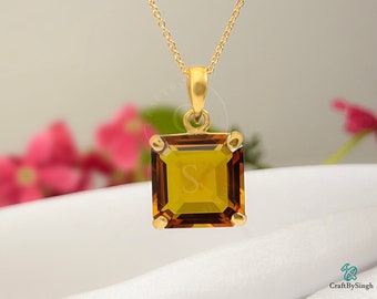 May include: A gold pendant necklace with a square-shaped, brown gemstone. The gemstone is set in a gold frame and has a slight sparkle.