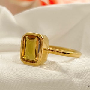May include: A gold ring with a large, rectangular, yellow gemstone set in a bezel setting.