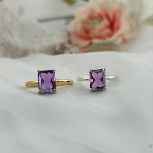 May include: Two rings with purple gemstone settings. The ring on the left has a gold band and the ring on the right has a silver band.
