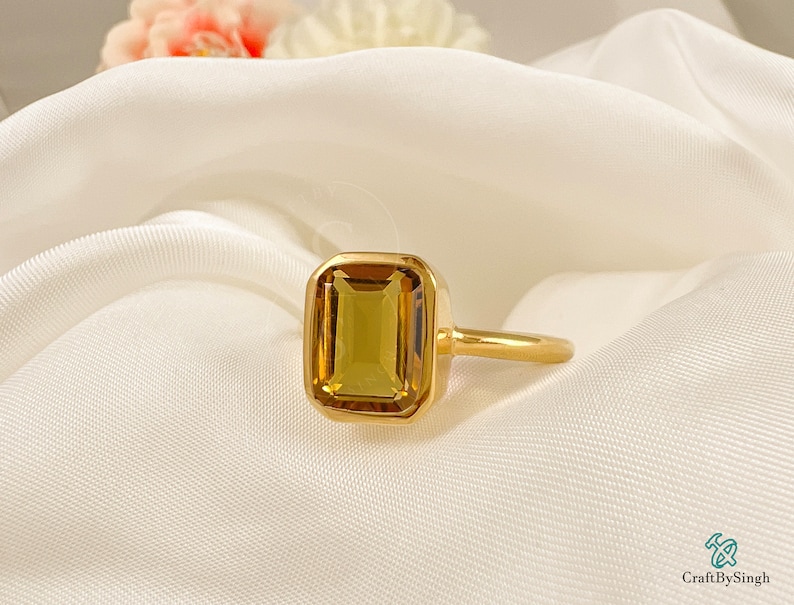 May include: A gold ring with a large, rectangular, yellow-brown gemstone set in a bezel setting.