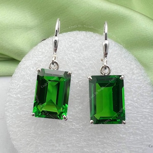 May include: A pair of silver dangle earrings featuring emerald green rectangular gemstones. The earrings have a simple design and are ideal for everyday wear.