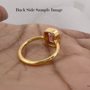 May include: A gold ring with a pink gemstone set in a square shape. The ring is on a hand, but the hand is not visible in the image.