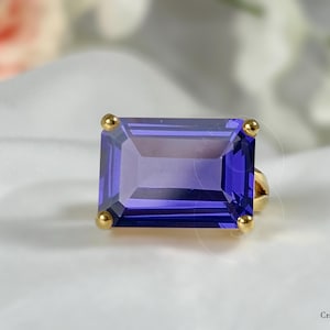 May include: A gold ring featuring a large, rectangular, purple gemstone.