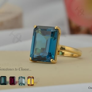 May include: A gold ring featuring a large, rectangular, teal gemstone. The ring has a simple, elegant design with a polished gold band. The image also shows a selection of other gemstones. Text on the image reads "15+ Gemstones to Choose..."