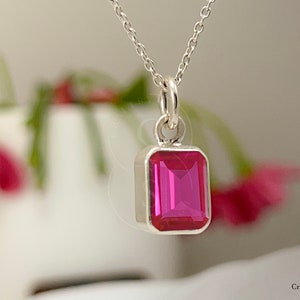 May include: A silver necklace with a pink gemstone pendant. The pendant is a rectangular shape with a faceted gemstone.