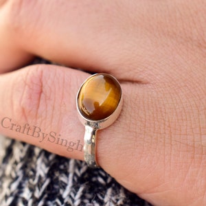 Op de afbeelding: Een zilveren ring met een bruine ovale tijgeroog-edelsteen. De ring heeft een gehamerde band.