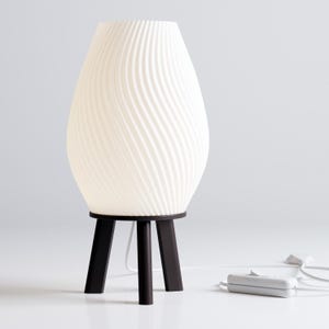 May include: A white table lamp with a wavy, textured shade and a black tripod base.