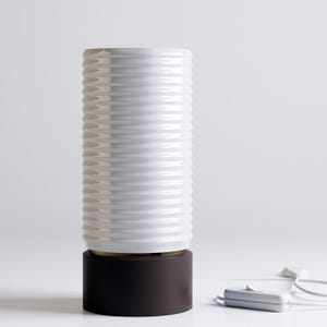 May include: White ceramic table lamp with a ribbed design and a black base. The lamp has a cord and plug.